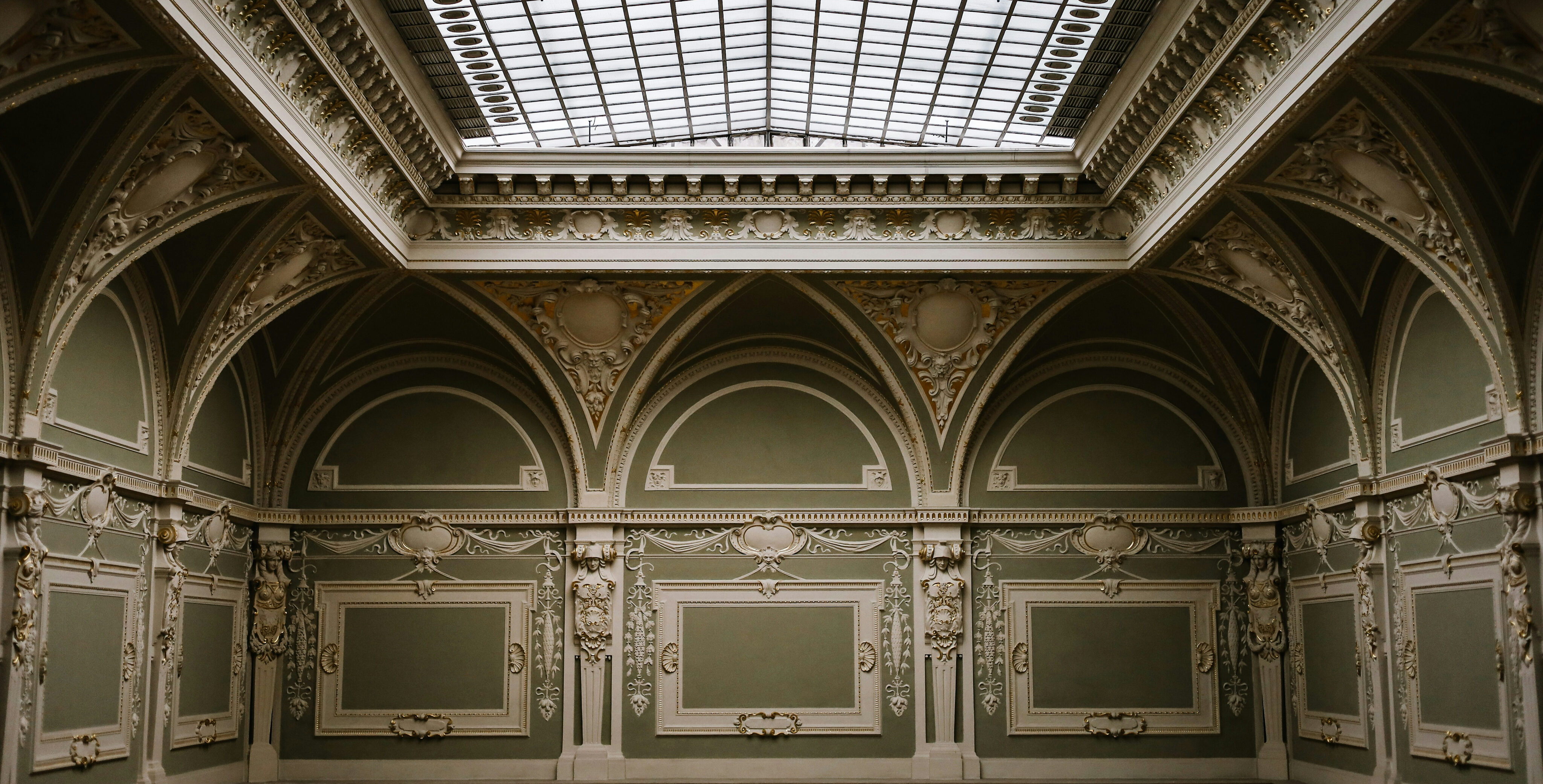 Image d'un hall au murs vert, architecture ancienne au mur, plafond de verre